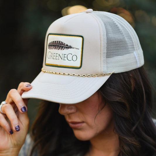 Model wearing beige GreeneCo women’s trucker hat with removable gold chain