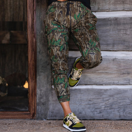 Women’s Mossy Oak camouflage joggers with gold drawstring end caps and grommet accents, designed for elevated athleisure wear and outdoor performance.
