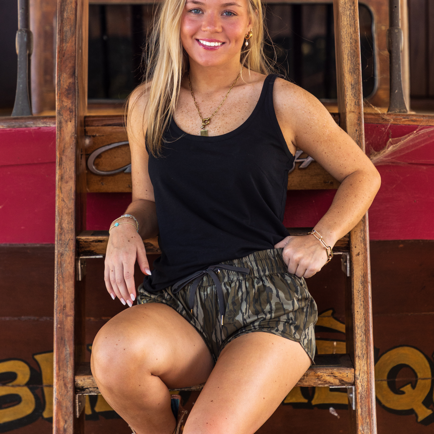 Woman sitting on a wooden staircase in GreeneCo Mossy Oak Bottomland shorts