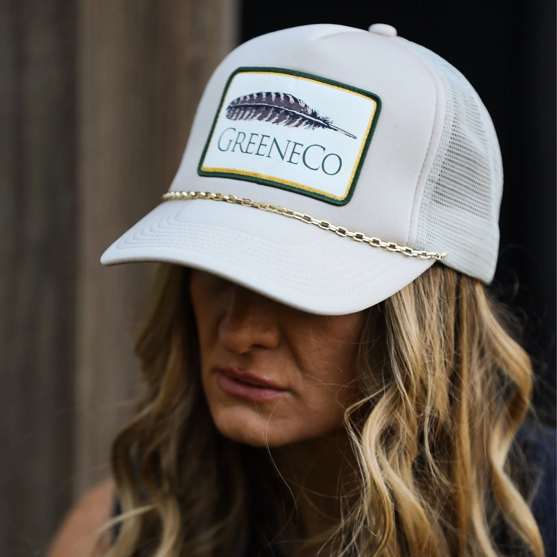 Side view of beige trucker hat with removable gold chain and branded feather by GreeneCo