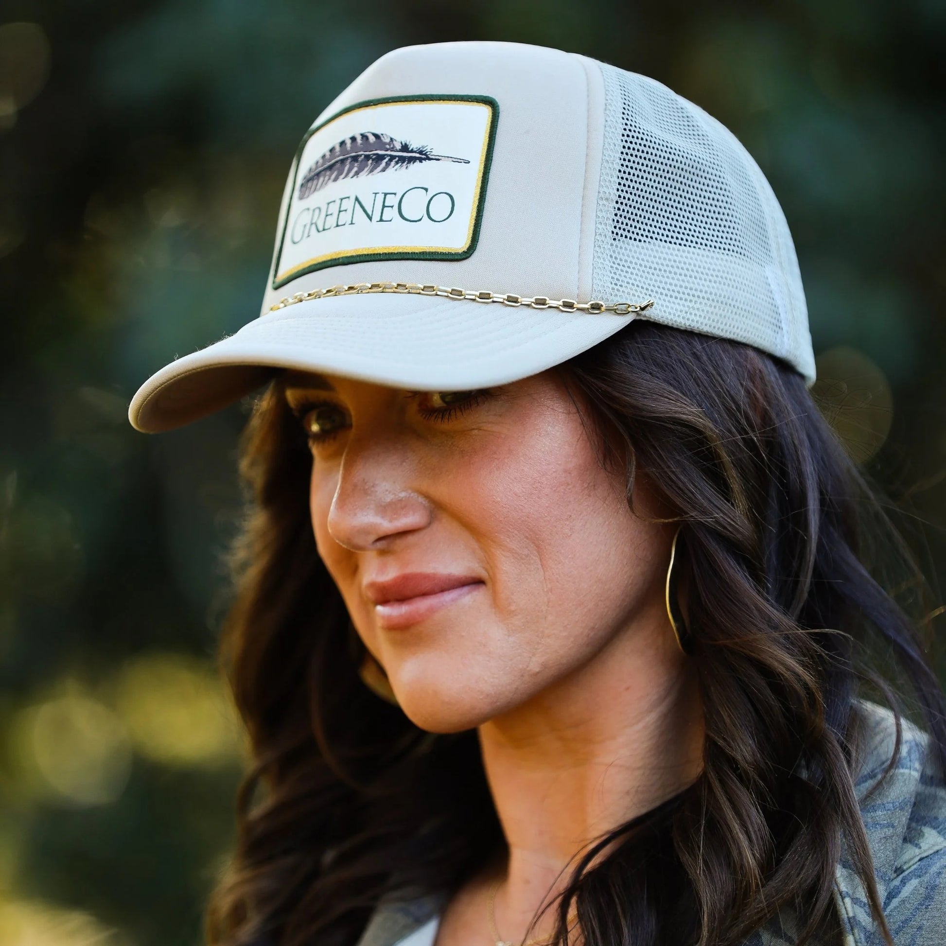 Removable gold chain on a beige trucker hat with GreeneCo branding and feather accent