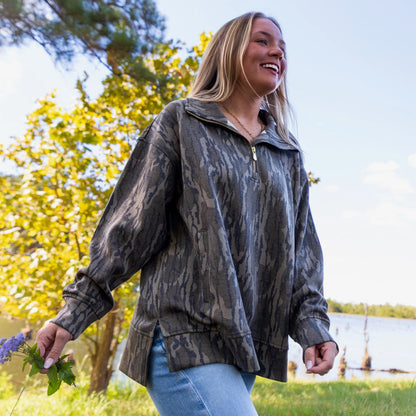 Model walking in Mossy Oak Bottomland 1/4 zip pullover showcasing movement and flexibility of longer back hem and drop shoulder style. Garment offers convenient welt pockets and oversized collar. 
