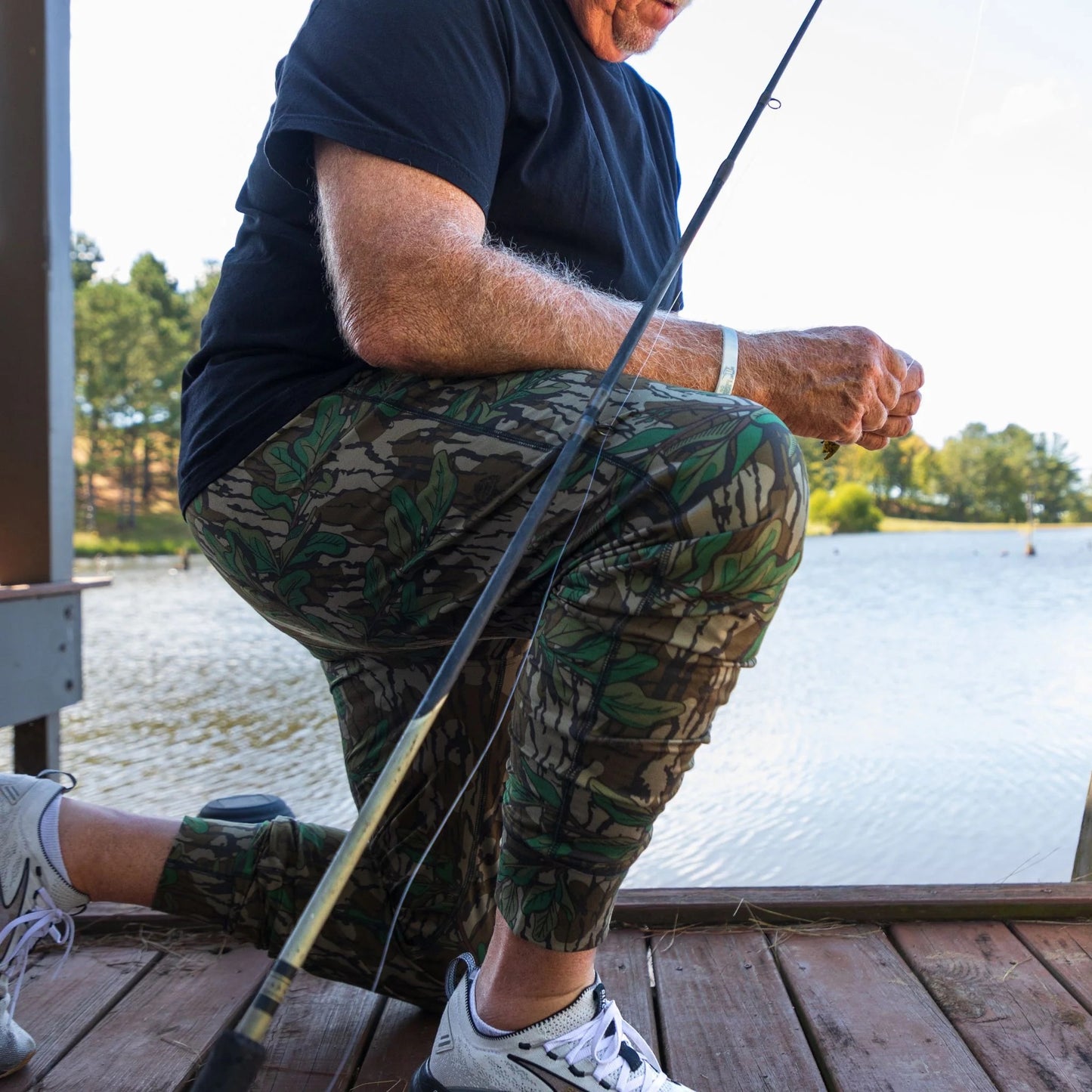 Model fishing on dock while wearing Mossy Oak Greenleaf joggers to showcase diverse styling options to wear.
