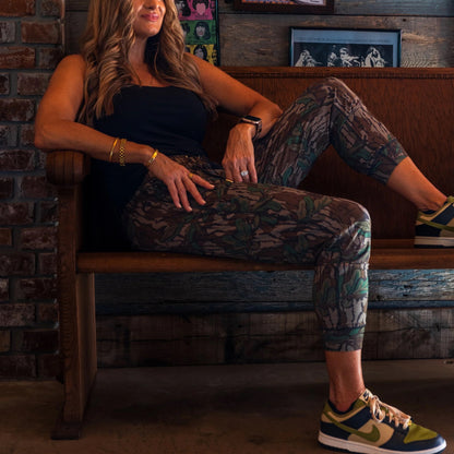 Woman sitting on a wooden bench wearing camo joggers in sneakers.