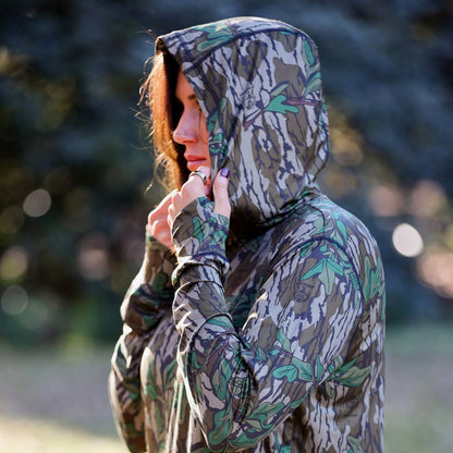 Side profile of model wearing women’s camo hooded performance top