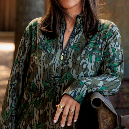 Close-up of women’s camouflage performance half zip top with leafy camo pattern and gold zipper detail, designed for outdoor and athleisure wear. 