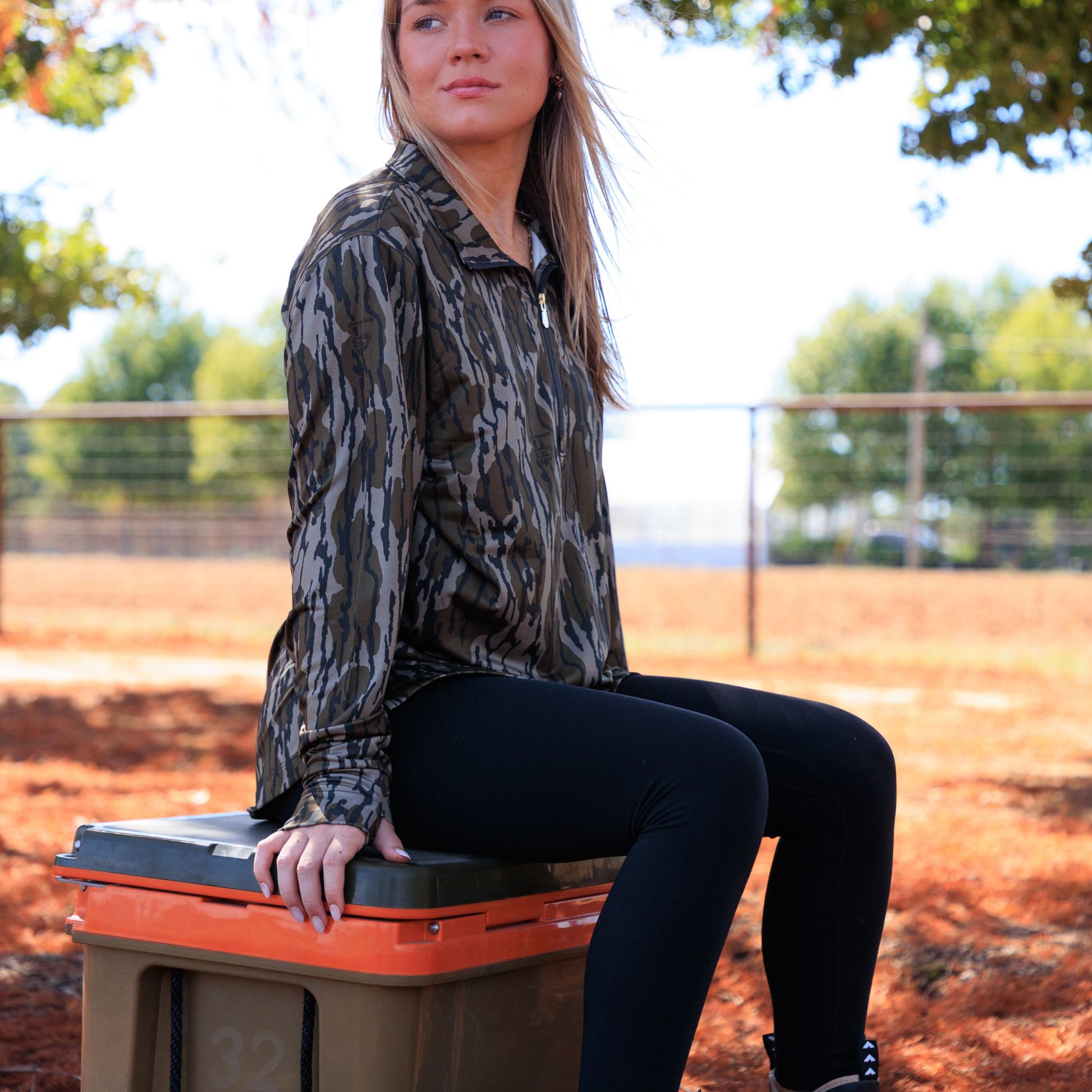 Women’s camouflage performance top sitting on outdoor gear, highlighting athletic fit