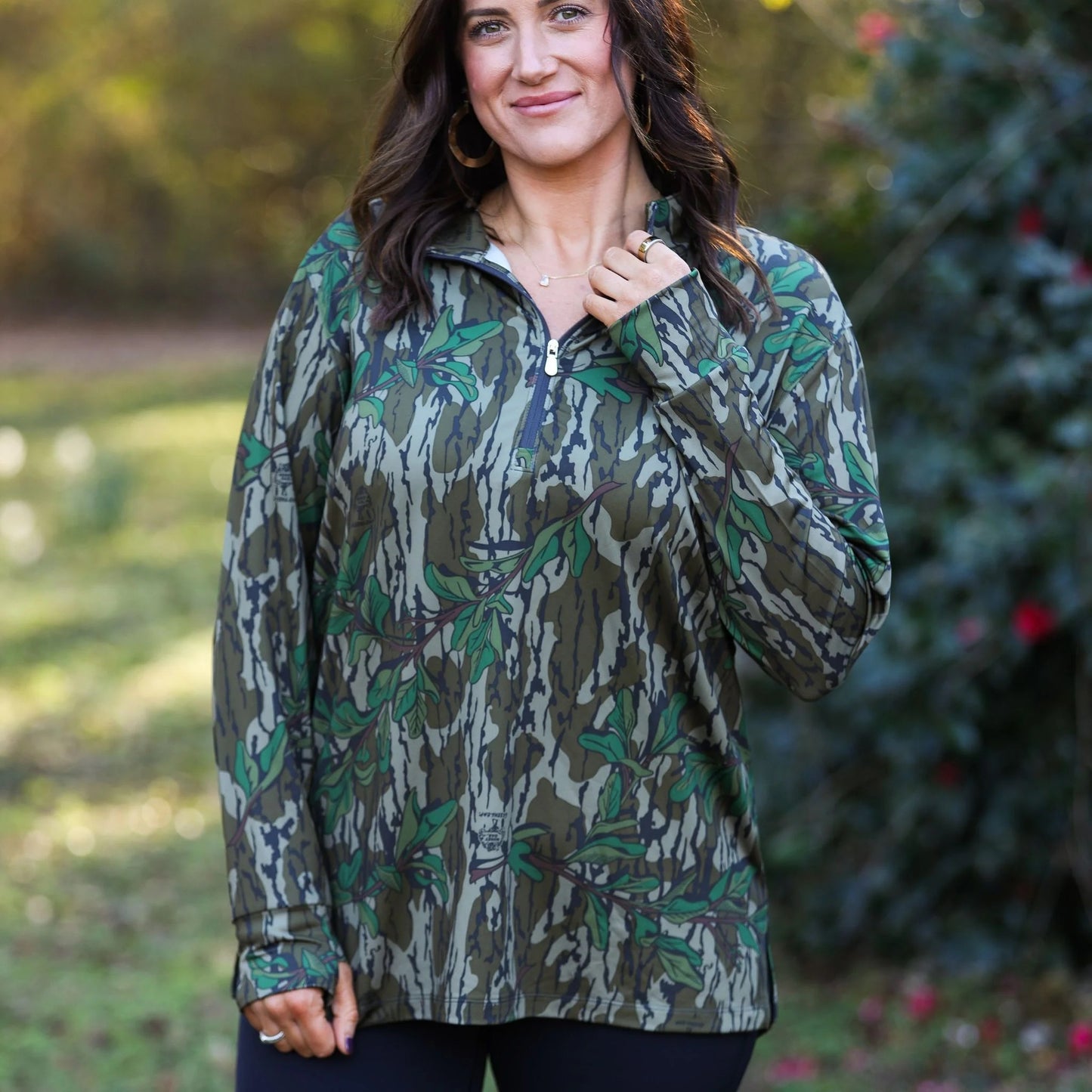Women’s camouflage top with gold zipper detail that shows outdoor versatility and athleisure fashion with performance blend fabric. Paired with black leggings.