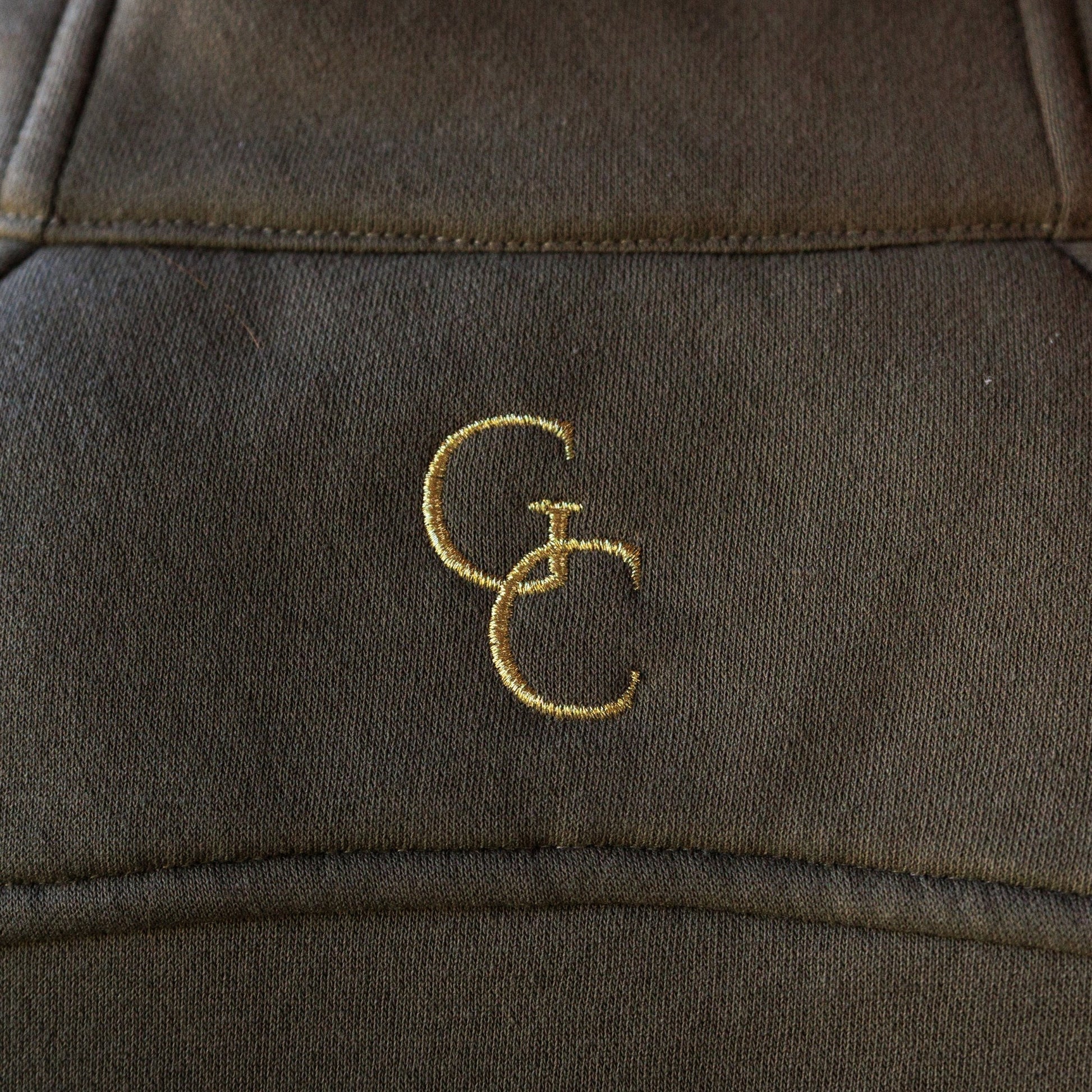 Close up detail of gold metallic embroidered GreeneCo logo on the back of a women’s pullover.