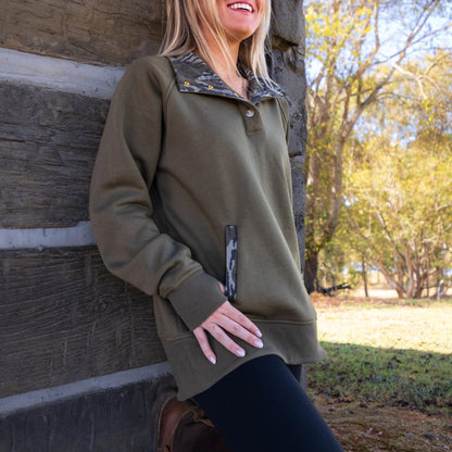 Model standing outside wearing an olive quarter-snap pullover with Mossy Oak Bottomland camouflage as accents throughout the garment. 